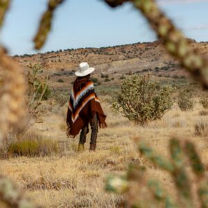 woman in red and black long sleeve shirt and white hat standing on brown grass field